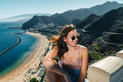 Young woman wearing sunglasses on beach against mountains