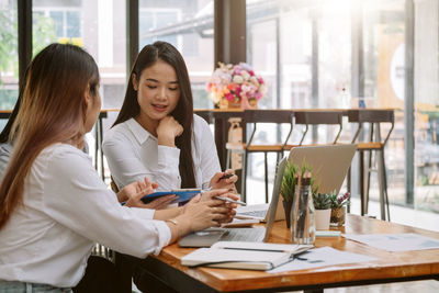Young woman using phone while sitting on table