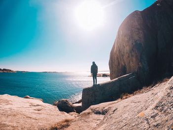 Man standing on rock by sea against sky