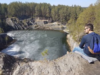 Rear view of man sitting on rock against trees