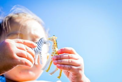 Low angle view of child holding toys against clear blue sky