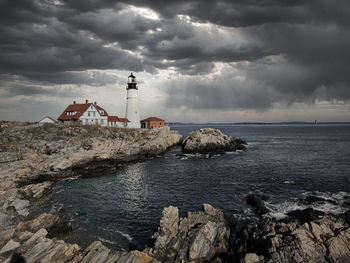 Lighthouse amidst sea and buildings against sky