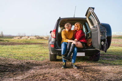Caucasian couple sitting in the trunk of a car looking at each other with love faces 