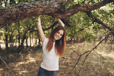 Portrait of smiling young woman standing on tree trunk