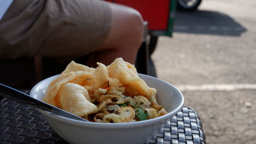 A white bowl of chicken porridge on a plastic chair at a street food vendor