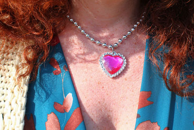 Neck detail of red-haired woman with pink heart pendant necklace and turquoise dress