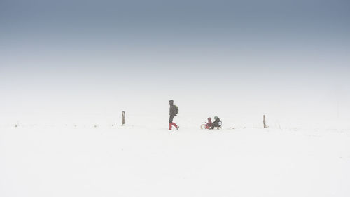Man pulling family on sled against sky