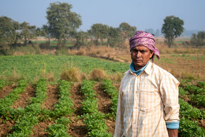 An indian farmer is standing in the vast grain field with a turban on his head. 