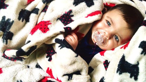 High angle portrait of baby sucking pacifier while wrapped in blanket