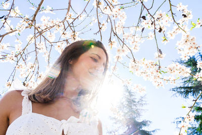 Portrait of young woman standing against cherry blossom tree