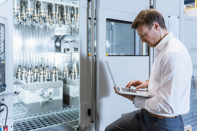 Businessman at machine in factory looking at laptop