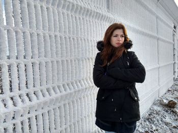 Young woman wearing warm clothing while standing by snow covered fence during winter
