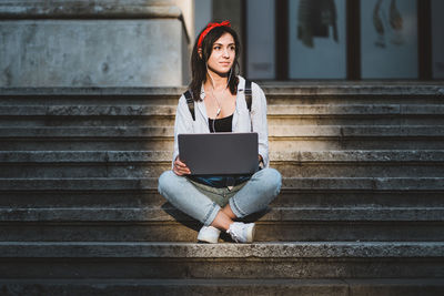 Young woman using laptop while sitting on staircase