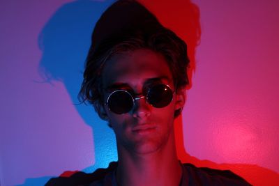 Portrait of young man wearing sunglasses in light against wall