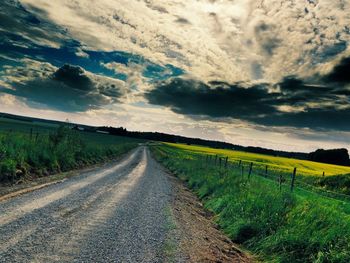 Road passing through field against cloudy sky