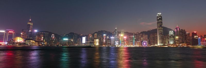 Illuminated city by river against sky