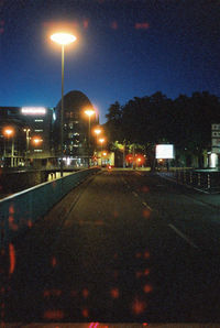 Illuminated street light by road against buildings at night