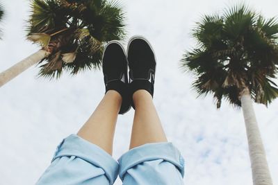 Low section of woman and palm trees against sky