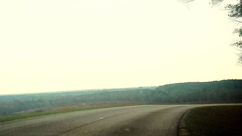 Road passing through field against clear sky