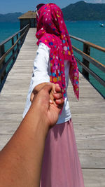 Midsection of woman holding umbrella while standing on pier