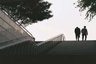 Rear view of people moving up on steps against clear sky