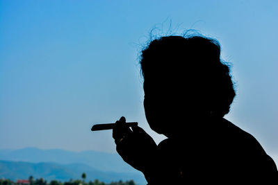 Portrait of silhouette man holding camera against blue sky