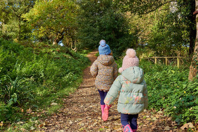 Rear view of women walking on footpath amidst plants