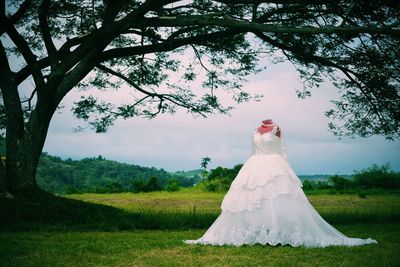 Woman standing on field by tree against sky