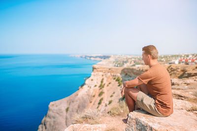Man sitting on rock by sea against sky