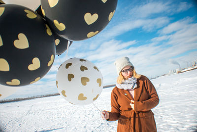 Woman holding balloons on snow covered land