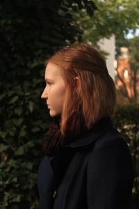 Side view of young woman standing against trees