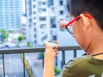 Close-up of boy holding navigational compass and pointing while standing by railing