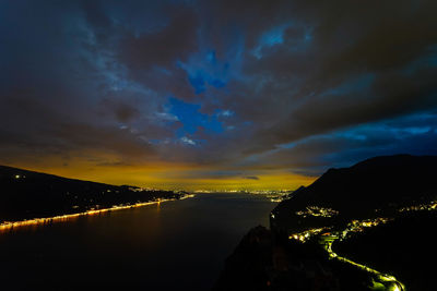 Illuminated city by sea against sky at night