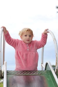 Portrait of cute girl sitting on railing against sky