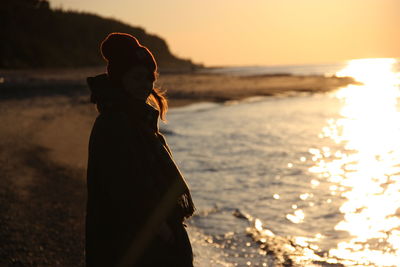 Side view of woman standing by shore during sunset