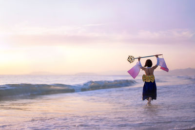 Rear view of young woman wearing costume holding wand at beach during sunset