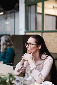 Thoughtful businesswoman sitting with hands clasped at table in creative office