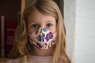 Close-up portrait of cute girl wearing mask standing at home
