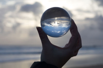 Close-up of hand holding crystal ball against sea