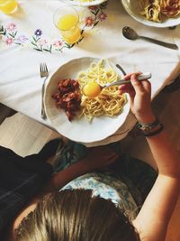 Directly above shot of person with egg yolk in spoon over pasta at home