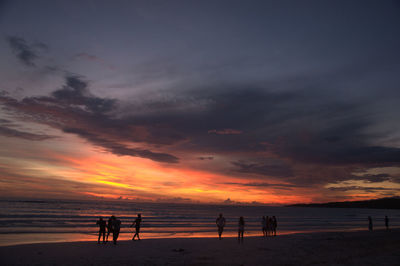 Silhouette people on beach against sky during sunset