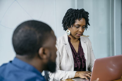 Businesswoman using laptop computer while sitting with colleague in office