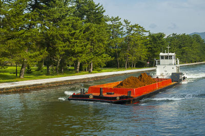 Boat on river by trees against sky