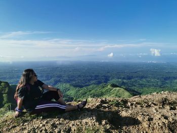 Woman sitting on mountain against sky