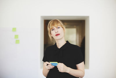 Portrait of confident businesswoman holding sticky note pad in office