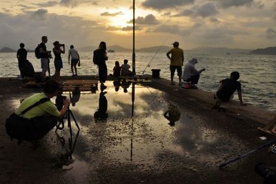 People at beach against sky during sunset