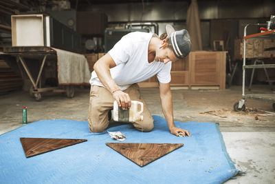 Carpenter pouring oil on triangle shaped wood at workshop