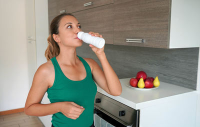 Portrait of young woman drinking whey protein beverage. home fitness girl drinks kefir from bottle.