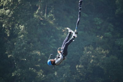 Man hanging on rope against trees