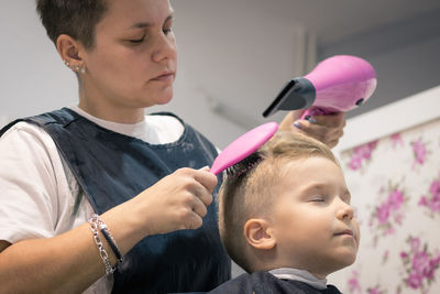 Barber blow drying hair of boy sitting on chair at shop